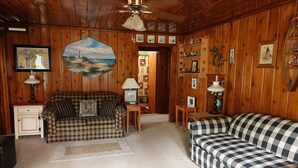 Una habitación acogedora con paredes de madera, un sofá a cuadros, una pequeña mesa y una lámpara.