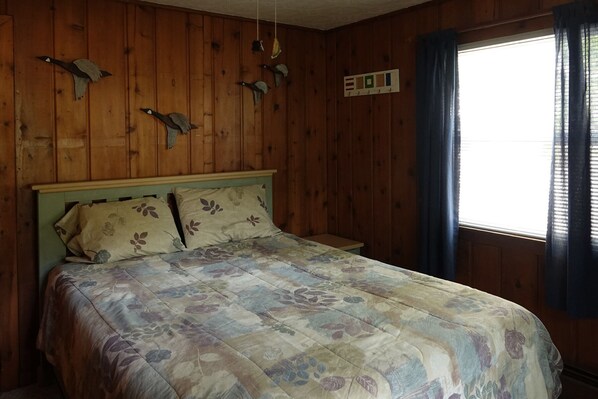 Un dormitorio con pared de madera, una cama con ropa de cama floral y una ventana con cortinas.