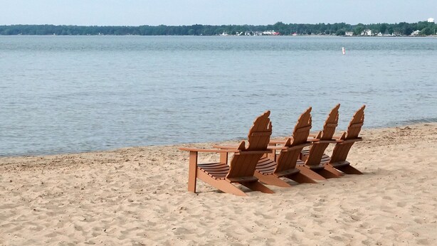 Una playa con sillas de madera tipo Adirondack y una mesa.