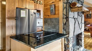 Eine Küche mit Holzausstattung, einem Edelstahl-Kühlschrank, einer schwarzen Granit-Arbeitsplatte und einem Kamin aus Stein.