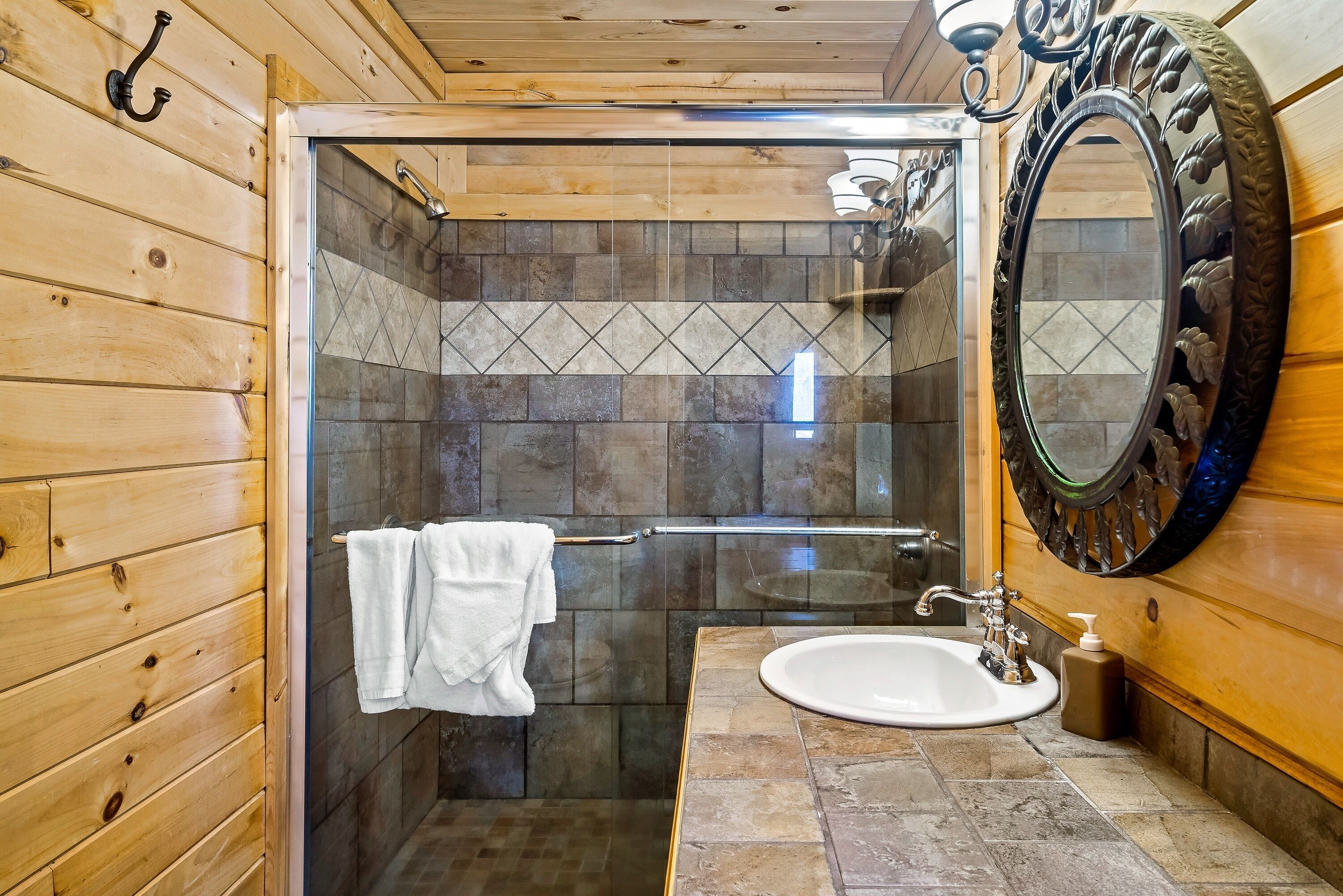 A wooden-paneled bathroom with a glass shower enclosure, a white sink, and a decorative mirror.