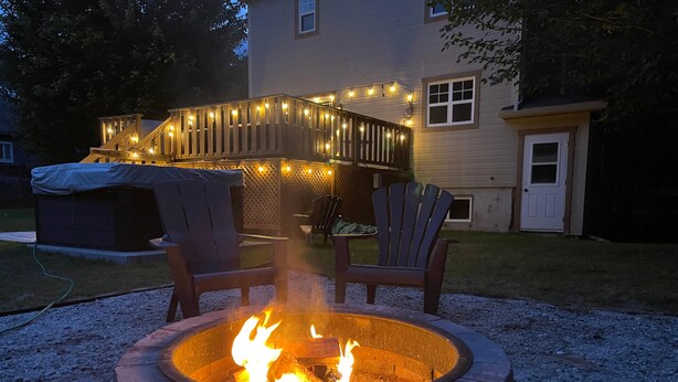 Een vuurplaats met twee stoelen, een overdekte barbecue en een terras met sfeerverlichting.