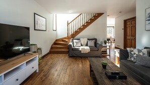 Een ruime woonkamer met een houten trap, een grote flatscreen televisie, een grijze bank en een houten salontafel.