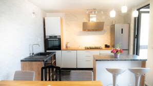 A modern kitchen with a built-in oven, a gas stove, and a microwave. There is a dining area with a wooden table and two bar stools.