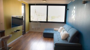 A living room with a sectional sofa, a hanging chair, a flat-screen TV, and a large window.