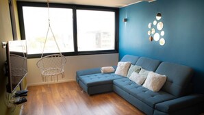 A modern living room with a sectional sofa, a hanging chair, and a large window providing natural light.