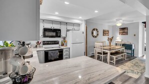 A modern kitchen with white cabinets, a marble countertop, and a dining area with a wooden table and chairs. - FANTASTIC 2 BR 2 Blocks to beach pool balcony (Seaside Heights)