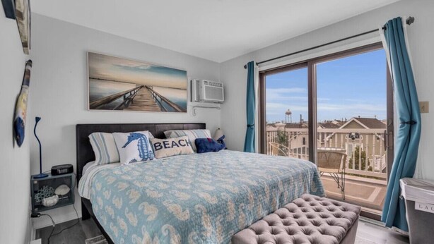 A bedroom with a large bed, a view of the city through a balcony, and a painting of a pier on the wall. - FANTASTIC 2 BR 2 Blocks to beach pool balcony (Seaside Heights)