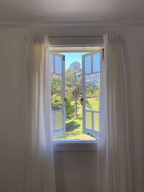 Una ventana abierta con cortinas blancas, mostrando una vista de un paisaje verde y árboles.