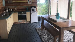A rustic kitchen with wooden walls, a wooden table, and a view of greenery outside. - Byron Bay hinterlands vintage-styled nature oasis! (Myocum)