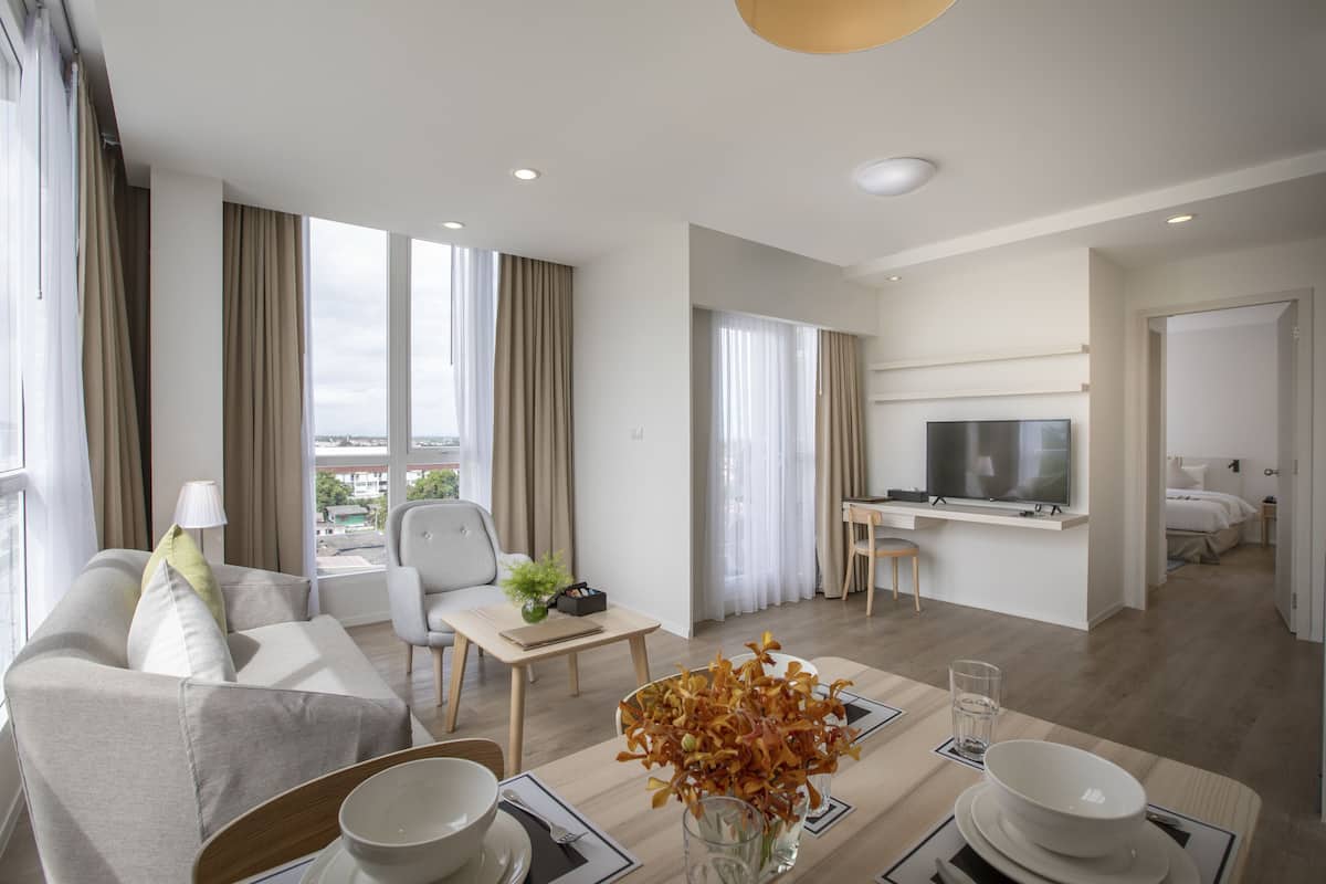 Een moderne hotelkamer met een bank, eettafel, televisie en uitzicht op de stad.