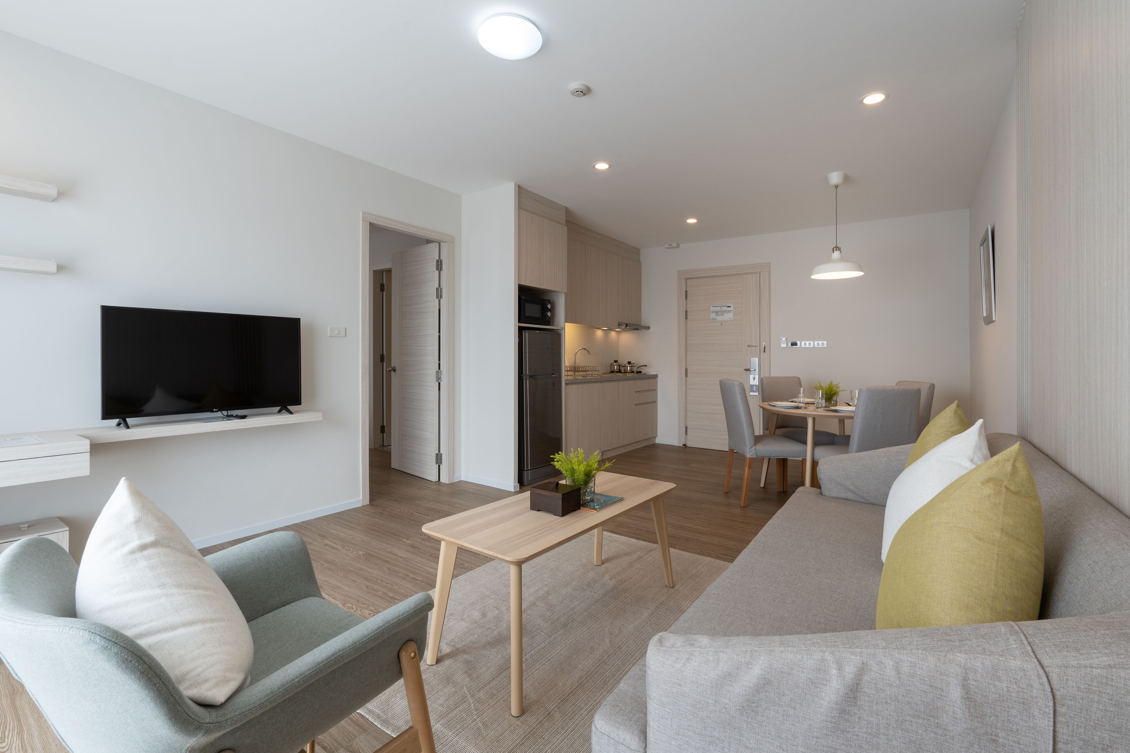En moderne stue med et fladskærms-tv, en sofa, et spisebord og et køkken med skabe og et køleskab.