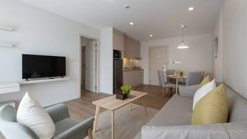 En moderne stue med et fladskærms-tv, en sofa, et spisebord og et køkken med skabe og et køleskab.