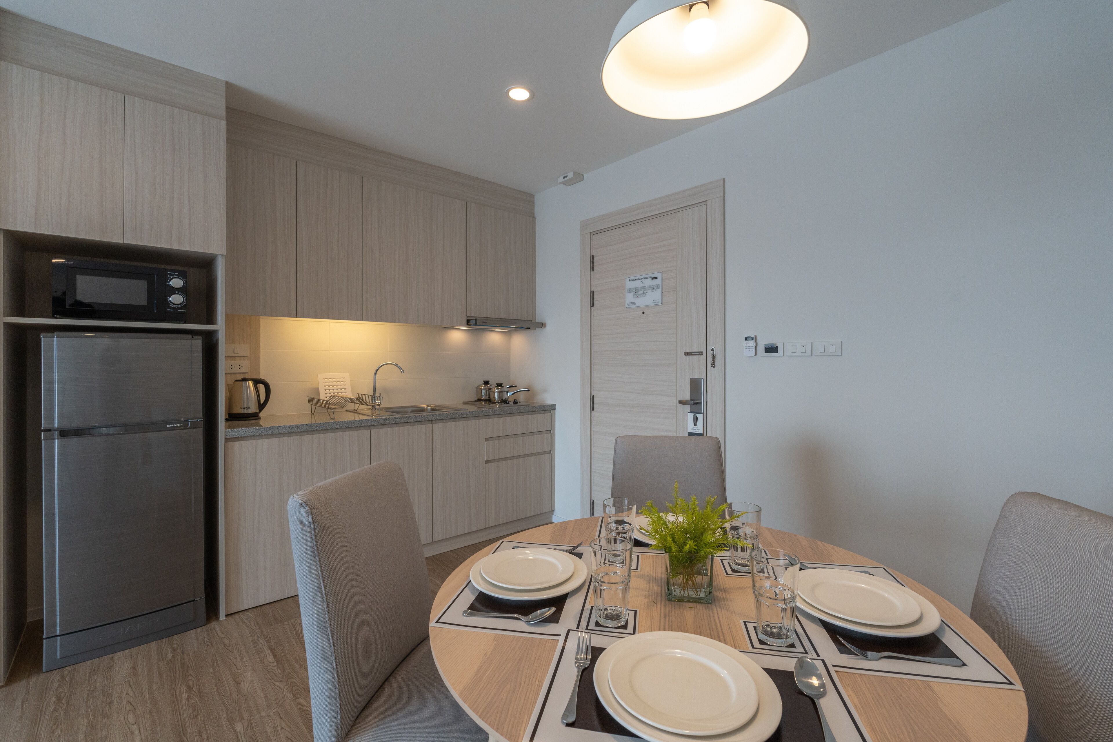 A modern kitchen with a built-in microwave and oven, a dining table set with plates and glasses, and a light fixture above.