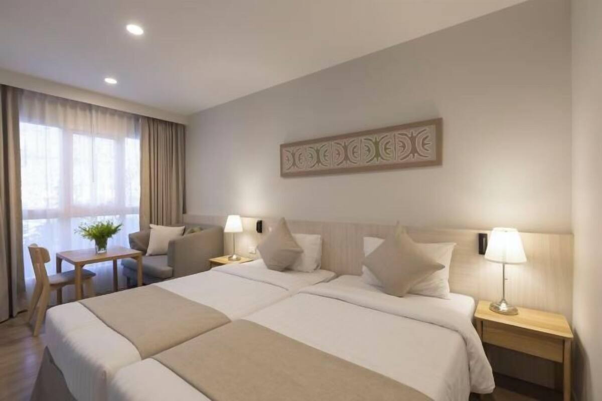 Een hotelkamer met een groot bed, twee nachtkastjes, een bureau met stoel en een raam met gordijnen.