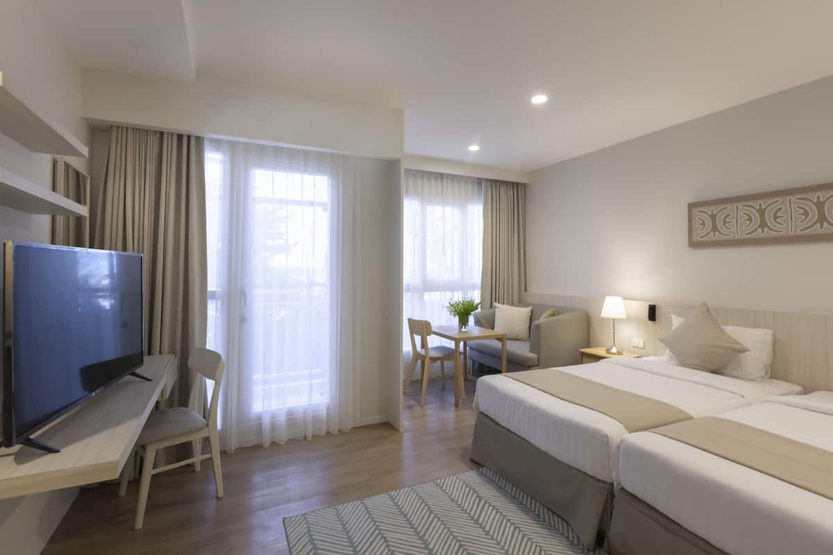 Hotelkamer met een bed, een bureau met een televisie, een stoel, een kleine tafel met een plant en een lamp.