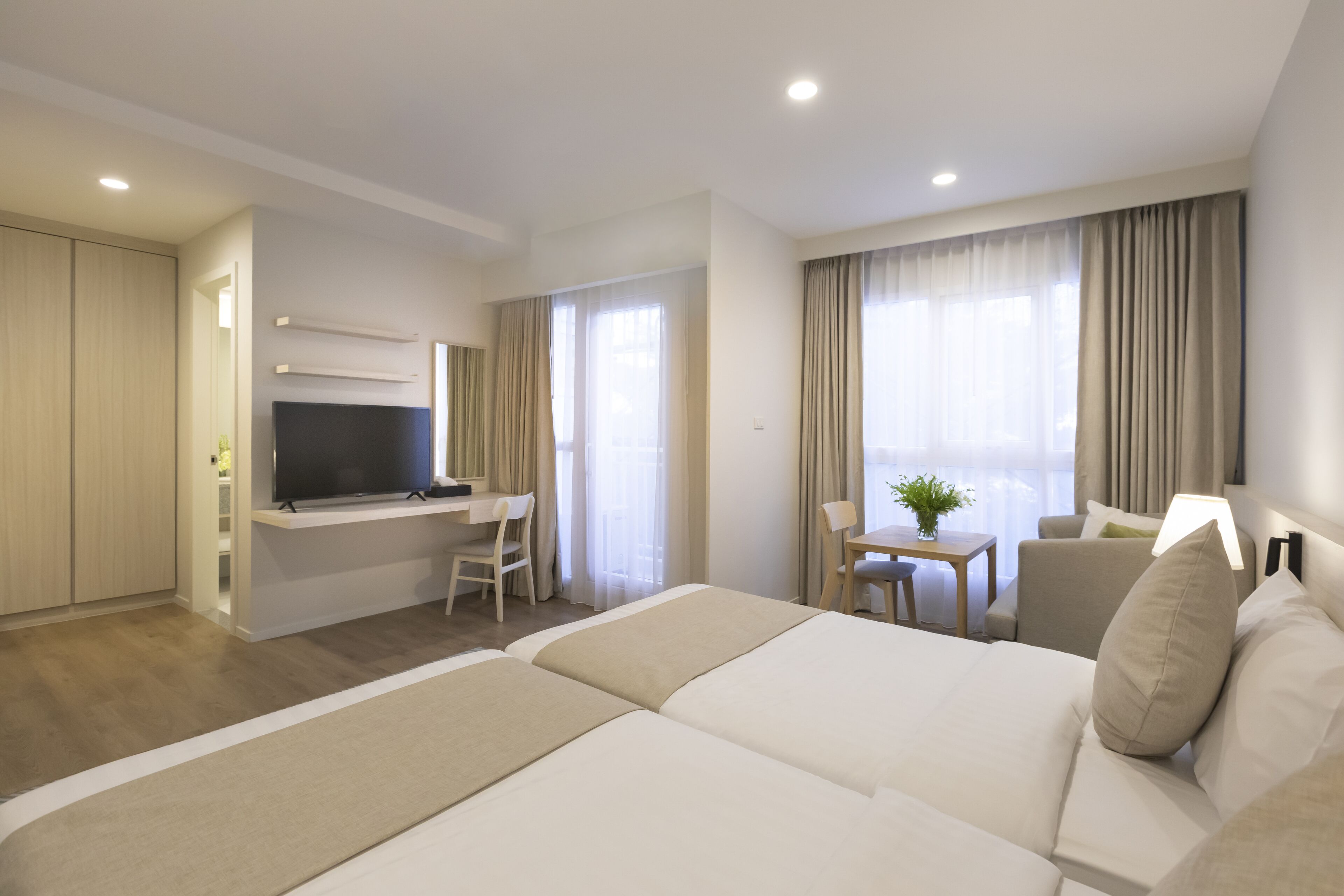 Una habitación de hotel con una cama grande, un escritorio con televisor, una mesita con una planta y un sofá.