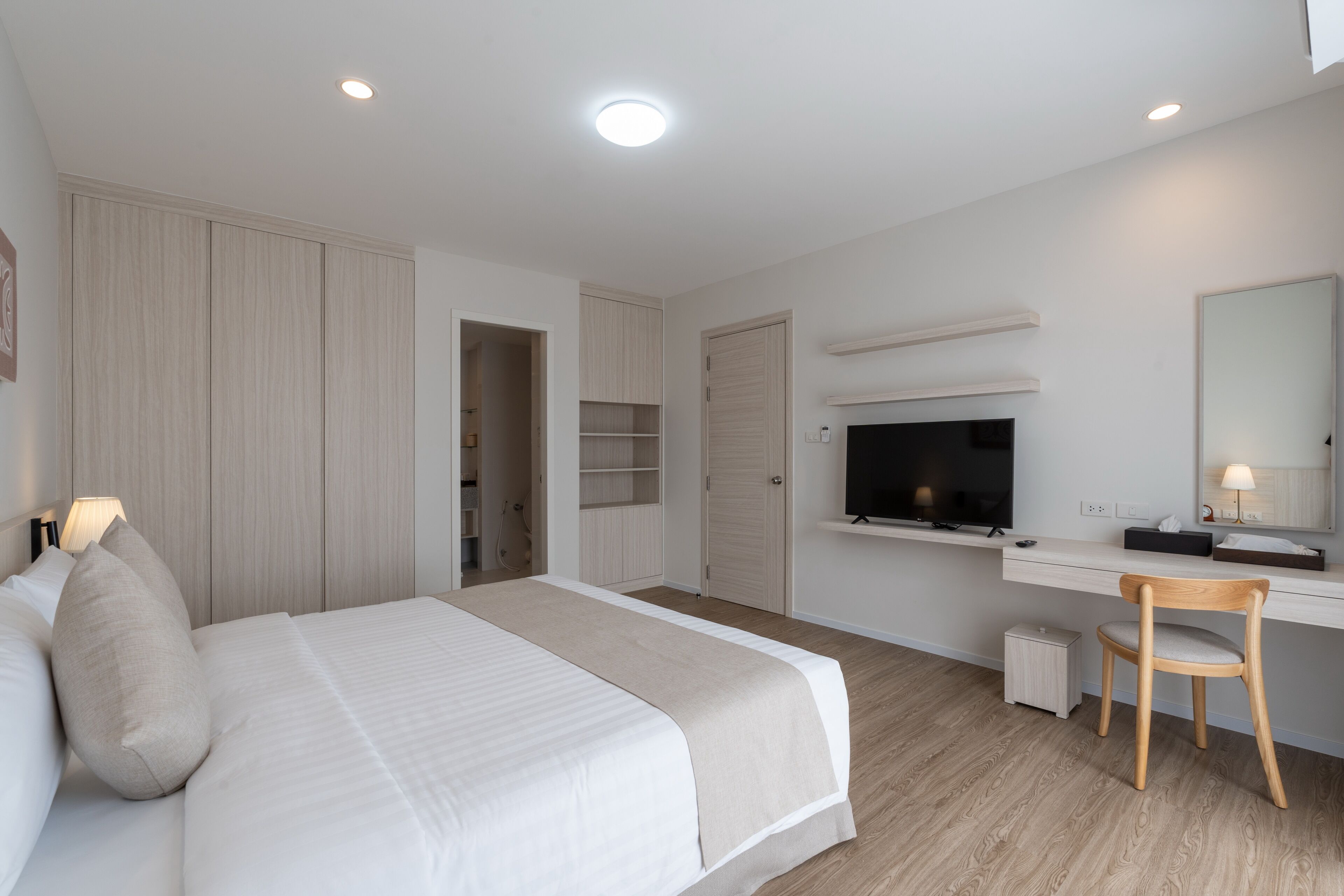 Una habitación de hotel moderna con una cama grande, un escritorio, un televisor y un espejo.