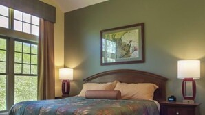 A room with a bed, two bedside lamps, a painting on the wall, and a window with curtains. - Luxury Resort in Shenandoah Valley (McGaheysville)