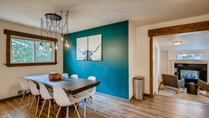 Een eethoek met een houten tafel en witte stoelen, een blauwe accentmuur en een open haard op de achtergrond.