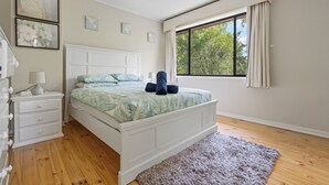 Une chambre à coucher avec un lit, une table de chevet, une commode et une fenêtre avec des rideaux.