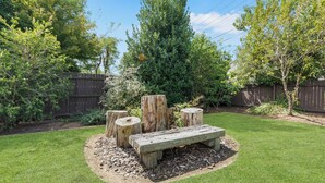 Un jardin bien entretenu avec un banc en bois, un espace de repos aménagé autour d’une souche d’arbre et une clôture en bois.