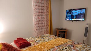 A hotel room with a bed, a TV on the wall, a bedside table, and a heater. - Vibrant apartment in the heart of the town (Edmundston)