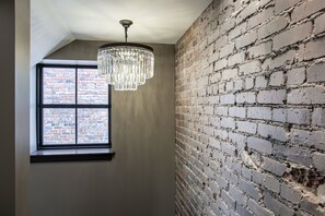 A room with a brick wall, a window with a view of a brick building, and a chandelier. - Luxury Lofts, near UNL, Arena, Stadium, prime location #203  (Lincoln)