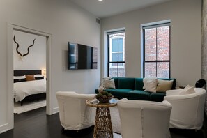 A modern living room with a green sofa, white armchairs, a small round table with a decorative bowl, a mounted TV, and a wall-mounted deer skull. - Luxury Lofts, near UNL, Arena, Stadium, prime location #203  (Lincoln)