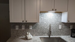 A kitchen with granite countertops, white cabinets, a stainless steel sink, and a coffee maker. - Blissful Villa, King Bed (Hilton Head Island)