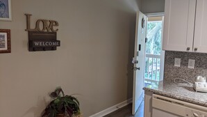 A hallway with a welcome sign, a plant, and a view into a kitchen area. - Blissful Villa, King Bed (Hilton Head Island)