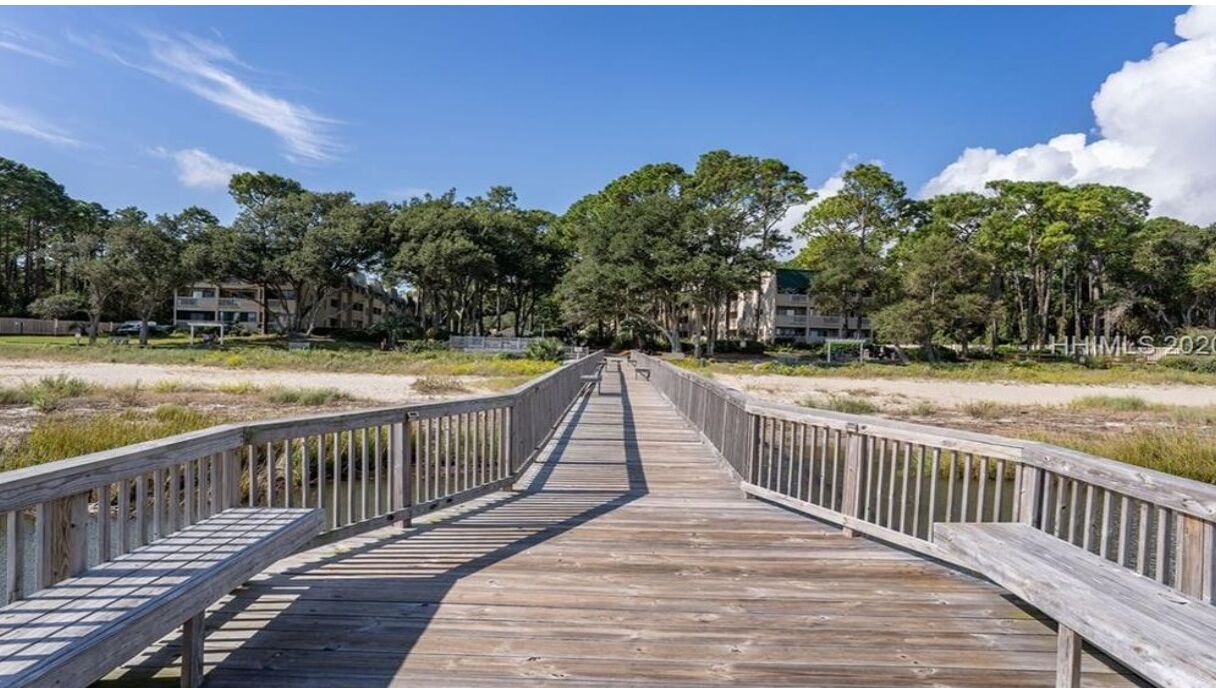 A wooden boardwalk leading to a building complex surrounded by trees.