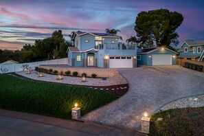 A two-story house with a garage, surrounded by a landscaped garden and a driveway. - Beautiful New Home with Large Balcony & Views!  (Escondido)