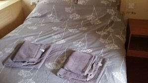 Een netjes opgemaakt bed met een bloemenprintdeken en twee gevouwen handdoeken erop.