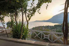 Une vue sur la côte, avec une clôture en bois, des palmiers et une montagne qui se dessine à l’horizon.