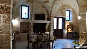 A stone-walled room with a fireplace, a dining table, and a television. - Holiday Home" C'era una Volta" (Torricella)