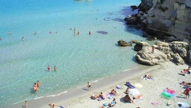 A beach with clear turquoise water, rocky formations, and people swimming and sunbathing. - Holiday Home" C'era una Volta" (Torricella)