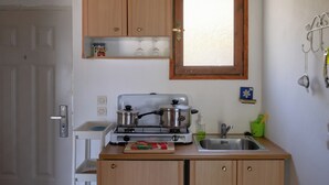 A compact kitchen with wooden cabinets, a gas stove, a sink, and a window above the sink.