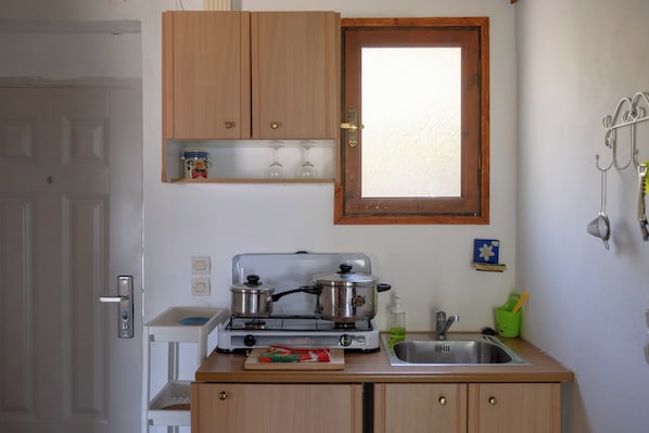 Eine kleine Küche mit Holzausstattung, einem Gasherd, einer Spüle und einem Fenster darüber.