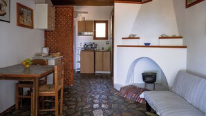 A compact kitchen with wooden cabinets, a dining table with chairs, and a stone floor.