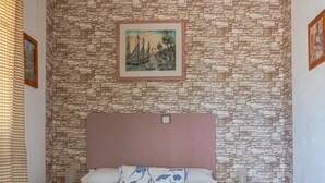 A bedroom with a stone-patterned wall, a wooden ceiling, a bed with a pink headboard, and a painting above the bed.