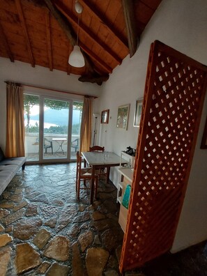 A room with a stone floor, wooden ceiling, a dining table with chairs, a sofa, a wooden partition, and a view through a glass door. - Astonishing House With sea View in Samos Island (Samos)
