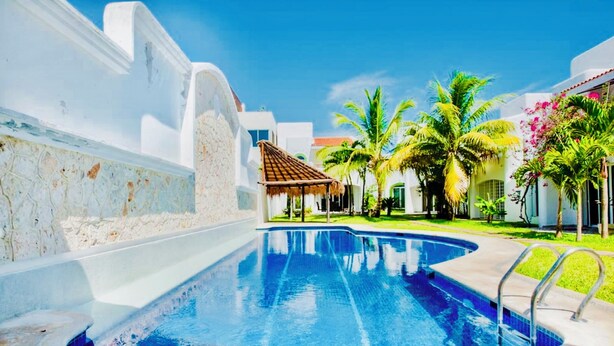 Una piscina con agua azul cristalina, rodeada de edificios blancos y palmeras.