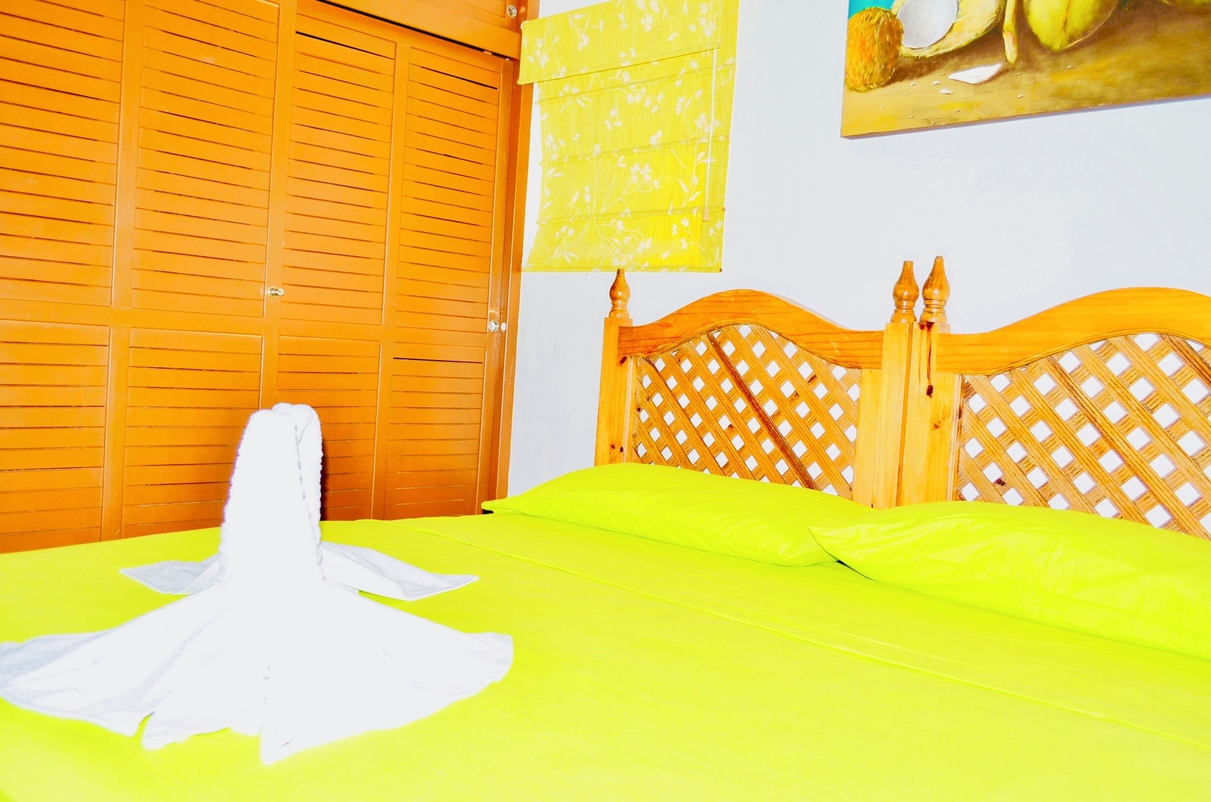 A bed with a bright yellow bedspread, a wooden headboard with a lattice design, and a wooden wardrobe with horizontal slats.