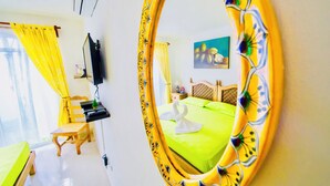 Una habitación de hotel con una cama verde, una silla de madera, un escritorio, un televisor y un espejo con marco floral.
