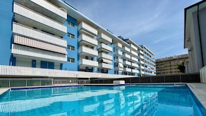 A swimming pool with a tiled deck, surrounded by a multi-story building with balconies. - Comfy Flat for Four-beahost (Caorle)