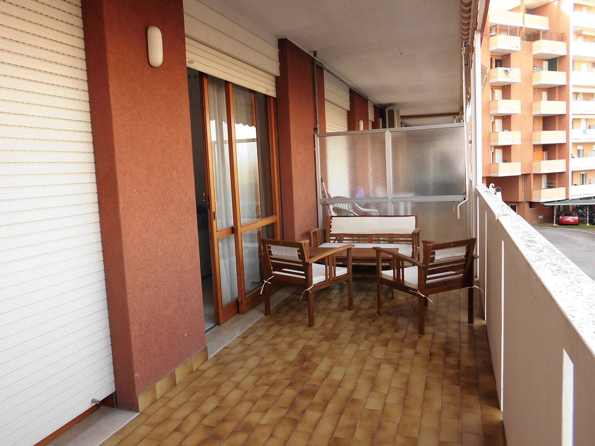 Un balcón con una mesa y sillas de madera, un ventanal corredero y vistas de un edificio residencial.