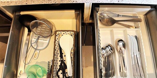 A drawer containing kitchen utensils including a strainer, spatula, whisk, and various spoons and knives.