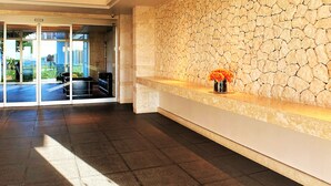 Un espace d’accueil avec un mur en pierre, un vase rempli de fleurs et une vue sur l’extérieur grâce à des portes vitrées.