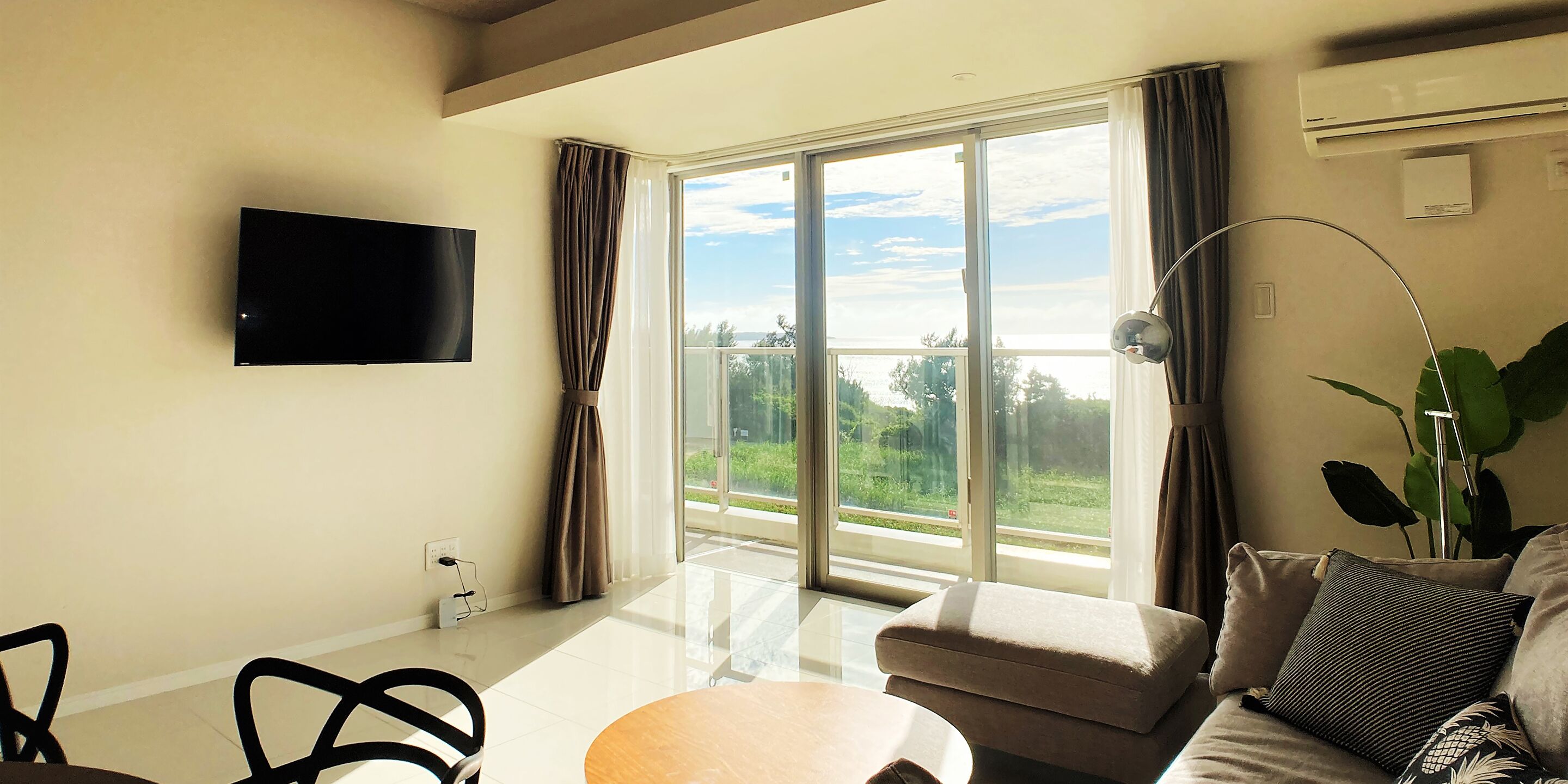 A modern living room with a flat-screen TV, a sofa, a coffee table, and a large sliding glass door leading to a balcony.
